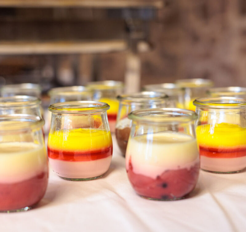 Mehrere kleine Gläser mit geschichtetem Dessert aus cremiger heller Masse und roter Fruchtsauce, teils mit gelber Fruchtcreme obenauf