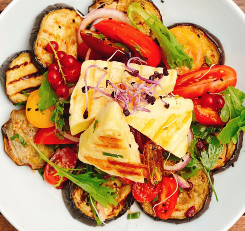 Gegrillte Halloumi-Scheiben mit gegrillten Auberginenscheiben, Cherrytomaten, roten Zwiebelringen und Rucola auf einem Teller